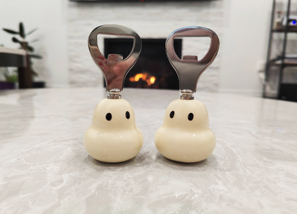 Two ghost-shaped bottle openers with metallic bottle openers on a light surface.