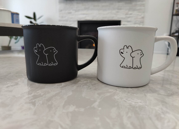 Black and white mugs with dog illustrations on a marble surface